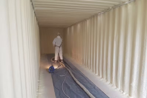 Aislamiento Térmico con Espuma de Poliuretano en Contenedor Marítimo Operario aplicando espuma de poliuretano proyectada en las paredes y techo interiores de un contenedor marítimo para aislamiento térmico en Santiago.