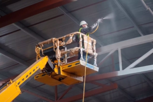 Operador industrial aplicando pintura técnica mediante sistema Airless en estructuras metálicas de techumbre para galpón industrial en Santiago de Chile.